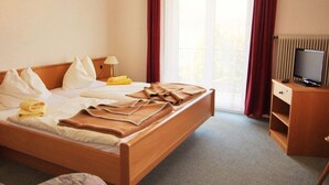 A hotel room with a bed, a television, a desk, and a window with curtains.