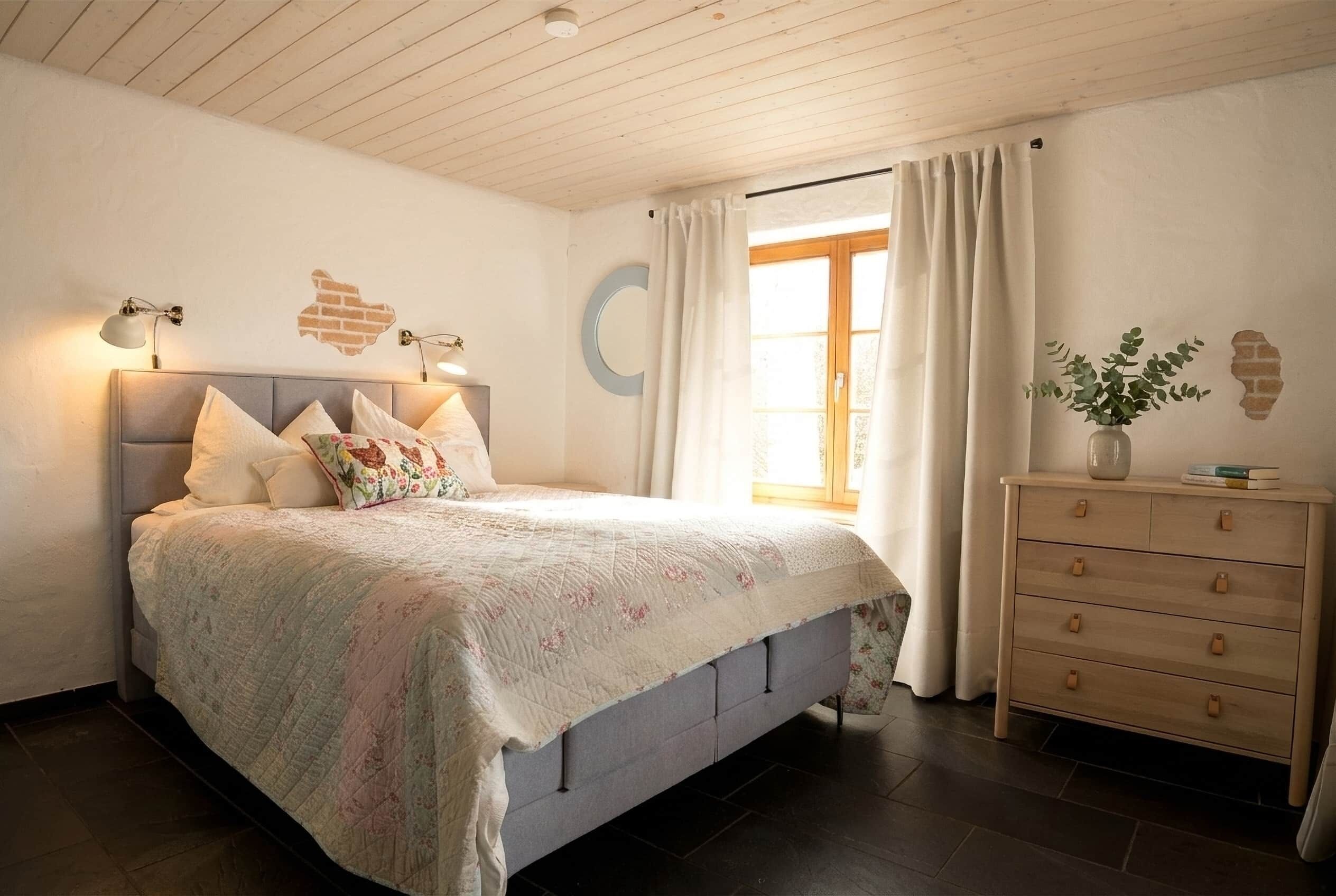 Ein Schlafzimmer mit Bett, Kommode, einem Fenster mit Vorhängen und Wanddekoration.