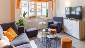Een moderne woonkamer met een grijze bank, oranje kussens, een klein rond tafeltje en een televisie.