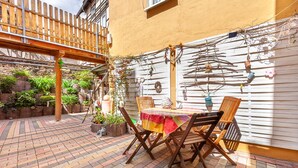 Een terras met een houten tafel en stoelen, een tegelvloer en een witte muur met decoraties.