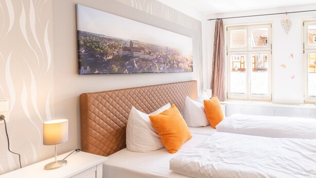 Een hotelkamer met een groot bed, een nachtkastje met een lamp, en een stadsgezicht schilderij aan de muur.