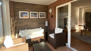 A sunlit patio with wicker furniture, a glass door leading to an indoor area, and a brick wall with framed pictures. - Holiday house near Baltic Sea (Bay of Lübeck) (Ahrensbök)