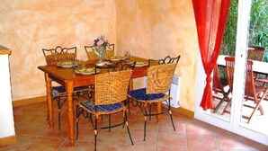 Een eetgedeelte met een houten tafel en rieten stoelen, een vaas met bloemen, en uitzicht op groen via een schuifdeur.