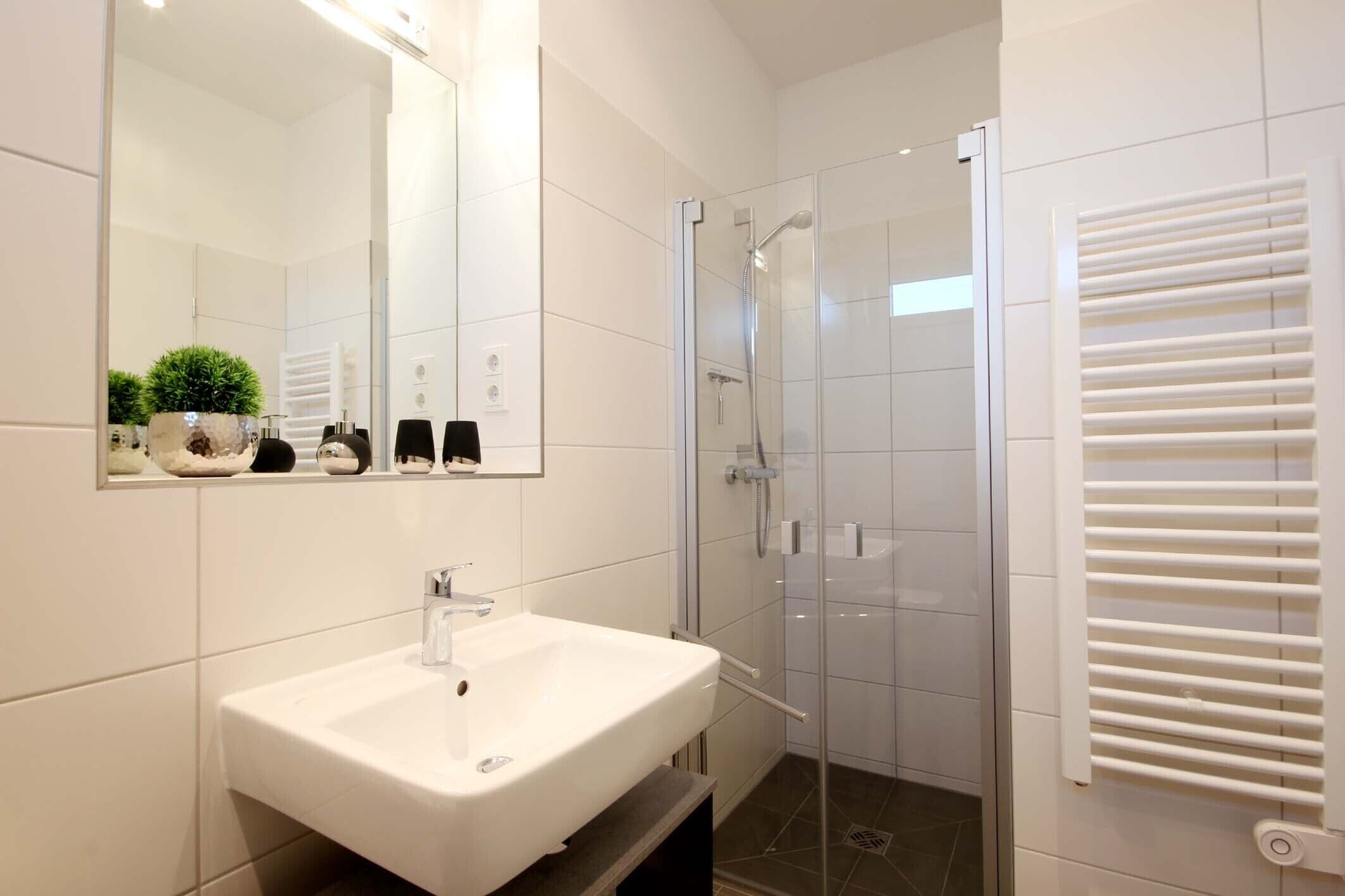 A modern bathroom with a white sink, a glass shower enclosure, and a towel rack.