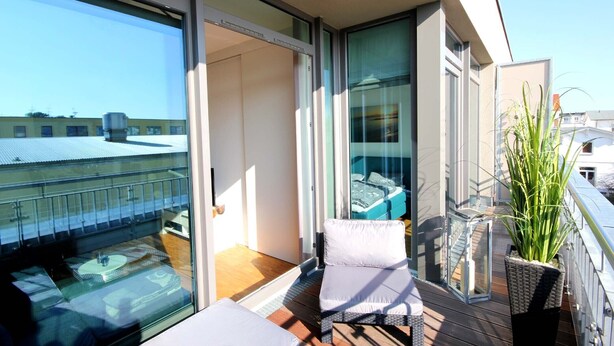 Ein Balkon mit Glastür, gepolstertem Sessel und einer Topfpflanze.