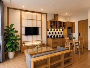 Una sala de estar moderna con una mesa de comedor de madera, un sofá, un televisor montado en la pared y una cocina con armarios de madera y un refrigerador.