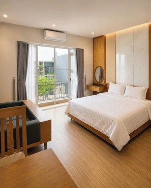 A hotel room with a bed, a desk, a chair, a window with curtains, and an air conditioning unit. - Minh Hưng Apartment (Da Nang)