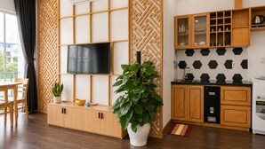 A modern living space with a flat-screen TV, wooden cabinets, a kitchen area, and a potted plant. - Minh Hưng Apartment (Da Nang)