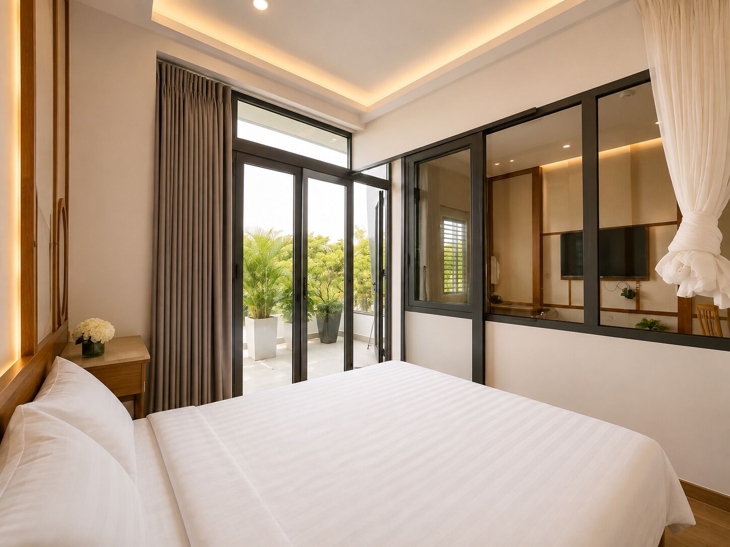 A hotel room with a large bed, a sliding glass door to a balcony, a flat-screen TV, and a large mirror.