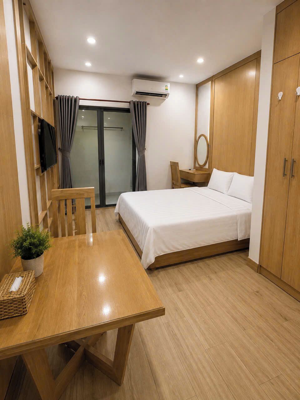 Quarto de hotel com cama, mesa de cabeceira, cadeira e pequena escrivaninha com espelho.