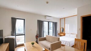 A modern hotel room with a sofa, a dining table, a TV, and a bed. - Minh Hưng Apartment (Da Nang)