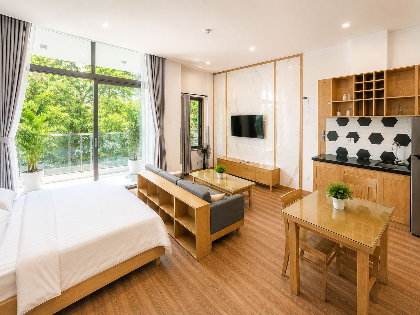 A modern hotel room with a large bed, a seating area, a dining table, and a kitchen area.