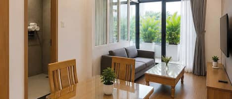 A modern living room with a wooden dining table, sofa, and a TV on a wooden stand.
