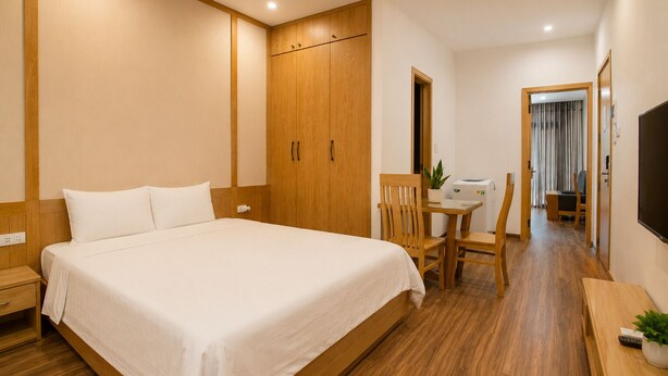 A hotel room with a bed, wooden wardrobe, a desk with a chair, a television, and a potted plant. - Minh Hưng Apartment (Da Nang)
