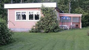 Une maison de plain-pied à la façade rose, dotée d’un porche abrité avec une table et des chaises, et d’un petit jardin.