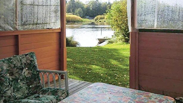 Une pièce avec vue sur un lac, une table recouverte d’une nappe à motifs floraux et une chaise agrémentée d’un coussin à fleurs.