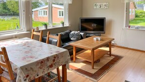 Un salon avec un canapé, une table, un téléviseur et une vue sur une maison par la fenêtre.