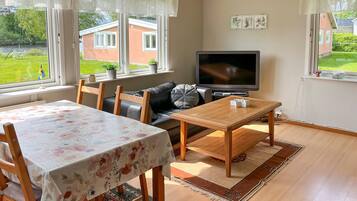 Ett vardagsrum med en soffa, ett bord, en tv och utsikt över ett hus genom fönstret.
