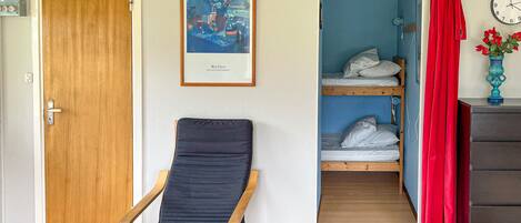 Ein Zimmer mit Holztür, einem gerahmten Gemälde, einem Etagenbett mit weißer Bettwäsche, einem roten Vorhang, einer Uhr und einer Vase mit Blumen.