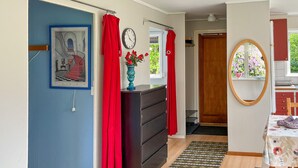 Une pièce avec un mur bleu, une porte en bois, une commode, un rideau rouge, une horloge, un vase avec des fleurs, un miroir et un tapis à motifs.