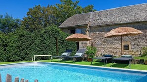 Ein Gebäude aus Stein mit Schwimmbecken, Liegestühlen und Reetdachschirmen.