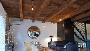 Ein gemütliches Wohnzimmer mit Holzboden, einem runden Spiegel, einem dunklen Sofa, einem Korbstuhl und einer Treppe im Hintergrund.