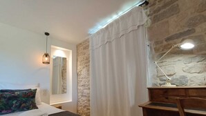 Ein Schlafzimmer mit Bett, Nachttischlampe, Holzstuhl, Steinwand und einem Fenster mit Vorhängen.