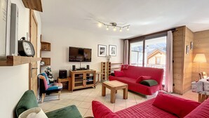 A cozy living room with a red sofa, a television, and a wooden cabinet. - Chamonix center, 64m², 6 pers., 2 bedr., parking (Chamonix-Mont-Blanc)