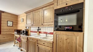 A kitchen with wooden cabinets, a stainless steel refrigerator, a microwave, and a tiled backsplash. - Chamonix center, 64m², 6 pers., 2 bedr., parking (Chamonix-Mont-Blanc)