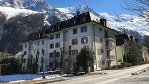 A multi-story hotel with a symmetrical facade, large windows, and balconies. It is situated in a mountainous area with snow-covered peaks in the background. - Chamonix center, 64m², 6 pers., 2 bedr., parking (Chamonix-Mont-Blanc)