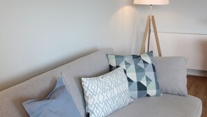 A grey sofa with patterned cushions and a floor lamp. - Modern flat facing south with view over mountains and lake (Murnau)