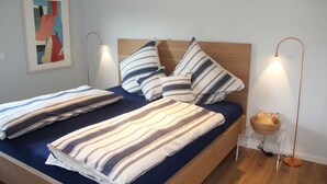 A neatly made bed with striped bedding, a framed abstract painting on the wall, and a bedside table with a lamp and a basket. - Modern flat facing south with view over mountains and lake (Murnau)