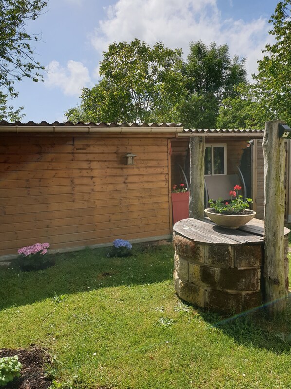 A wooden cabin with a tiled roof, a small garden area with flowers, and a stone well. - Chalet stay (Crécy-la-Chapelle)