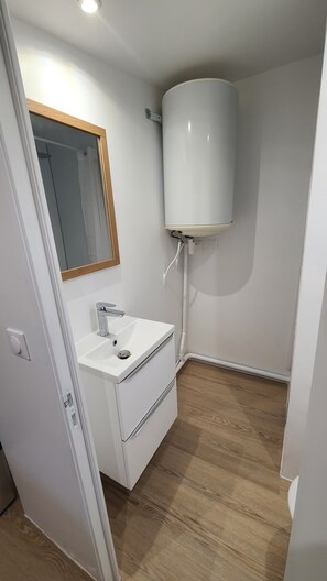 A small bathroom with a white sink, a mirror, and a white water heater mounted on the wall. - Chalet stay (Crécy-la-Chapelle)
