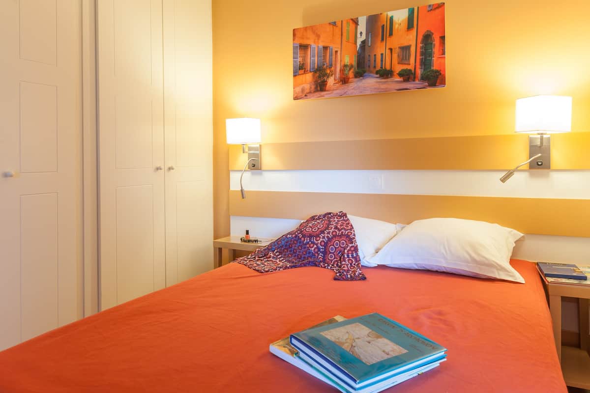 Une chambre d’hôtel avec un lit, deux lampes de chevet, un tableau au mur et une table de chevet avec un livre.