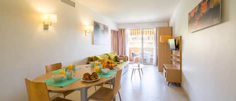 Ein Essbereich mit einem für das Frühstück gedeckten Tisch, inklusive Früchten und Gebäck, sowie einer Couch im Hintergrund.