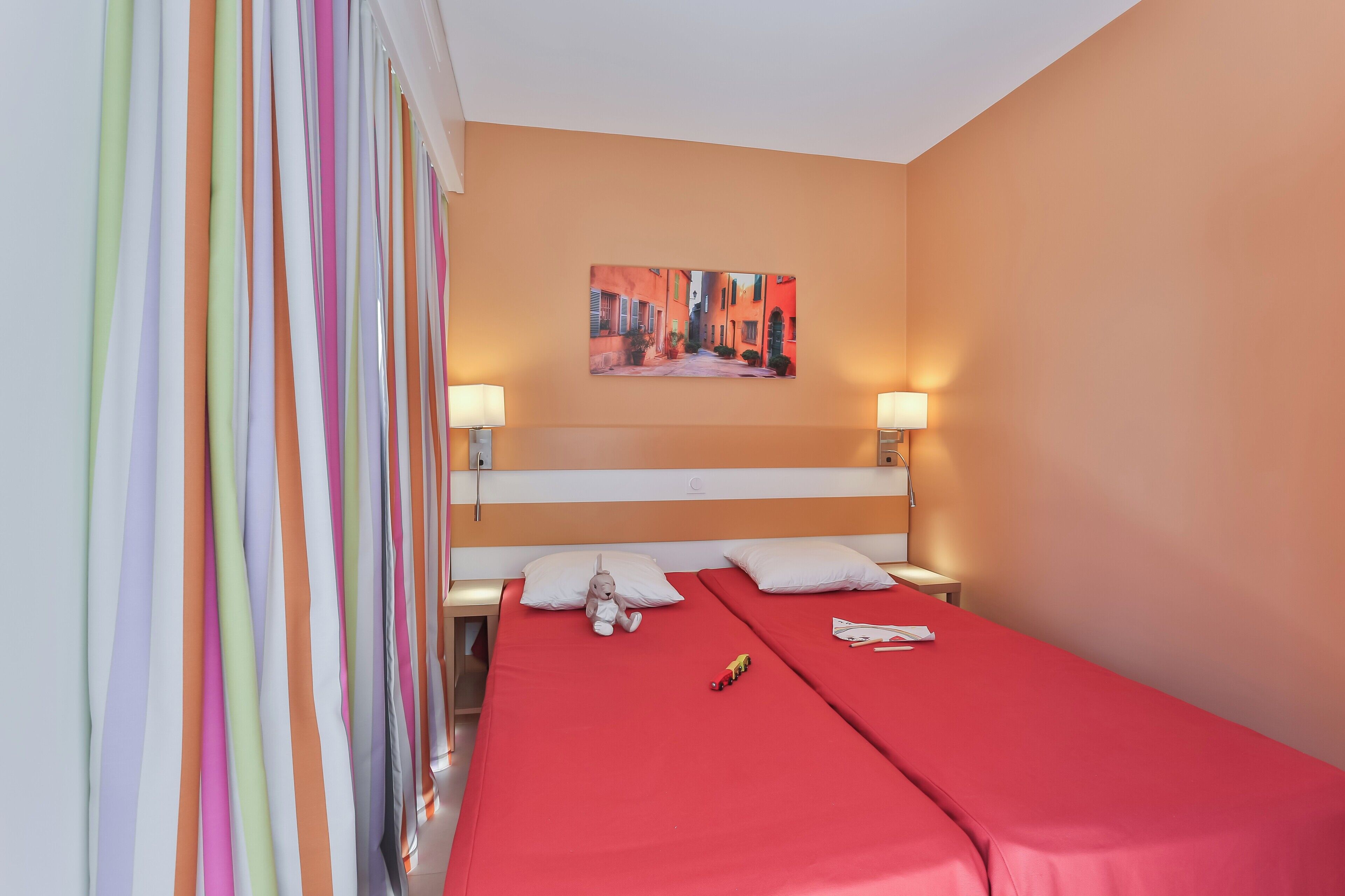 Une chambre d’hôtel avec deux lits, un tableau au mur et un rideau à rayures.