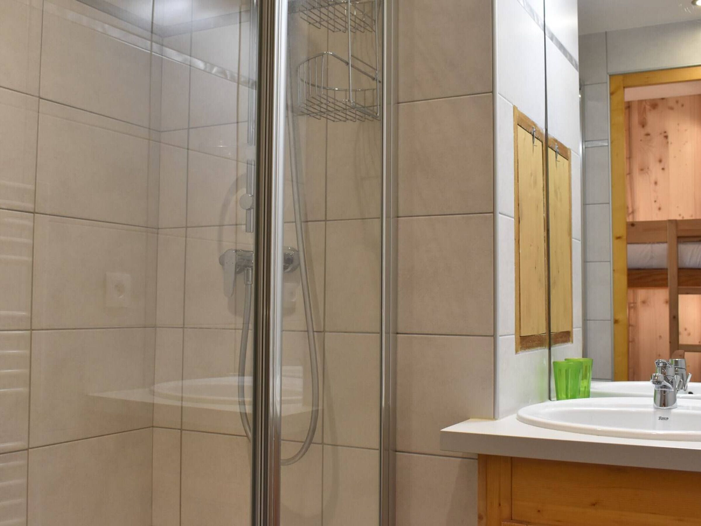 Un baño moderno con ducha acristalada, lavamanos blanco y muebles de madera.
