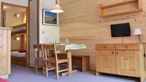 Ein gemütliches Zimmer mit einem hölzernen Etagenbett, einem Esstisch mit Stühlen, einer kleinen Kommode, einem Fernseher und einer Lampe.