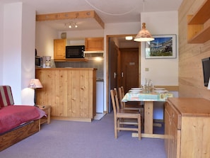 A compact kitchen with wooden cabinets, a microwave, and a coffee maker. There is a dining area with a table set for two, chairs, and a lamp.