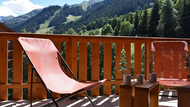 Ein Balkon mit zwei Stühlen und einem Tisch mit Blick auf eine Berglandschaft.