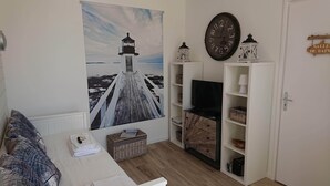 A cozy living room with a large painting of a lighthouse, a white sofa, a TV, and a wooden cabinet. - Our islands : Ile du Pilier - 200m Beach (Saint-Jean-de-Monts)