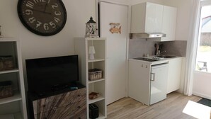 A compact living space with a TV, storage shelves, a small kitchen area with a sink and stove, and a clock on the wall. - Our islands : Ile du Pilier - 200m Beach (Saint-Jean-de-Monts)