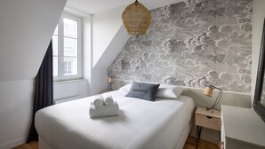 A modern bedroom with a large bed, a sloped ceiling, a decorative wall, and a bedside lamp.