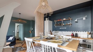 A modern kitchen with a dining area, featuring a wooden table set for four, white chairs, and a hanging light fixture.