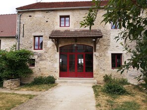 A stone building with a red door and windows, surrounded by greenery. - Large luxury gite 160 m2, capacity 6 adults + 3 children with spa (Montillot)