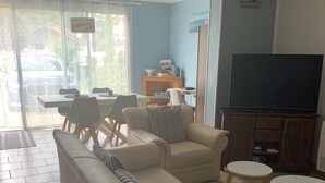 A living room with a sofa, armchairs, a TV, and a dining area with chairs and a table. - Bright house on large garden near beaches/town center/2 bicycles available (Soulac-sur-Mer)
