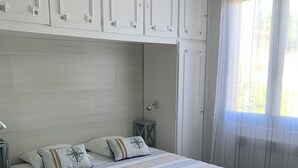 A bedroom with a bed, white cabinets, a hanging light fixture, and a window with curtains. - Bright house on large garden near beaches/town center/2 bicycles available (Soulac-sur-Mer)