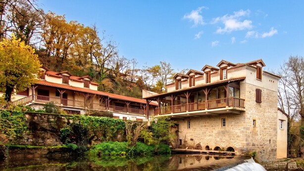 Un bâtiment historique, agrémenté d’une fontaine à l’avant, doté de murs en pierre et d’un balcon donnant sur l’eau.