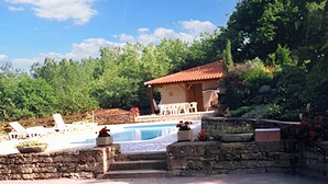 Un espace piscine avec des chaises longues, un mur en pierre et un bâtiment doté d’un toit rouge.